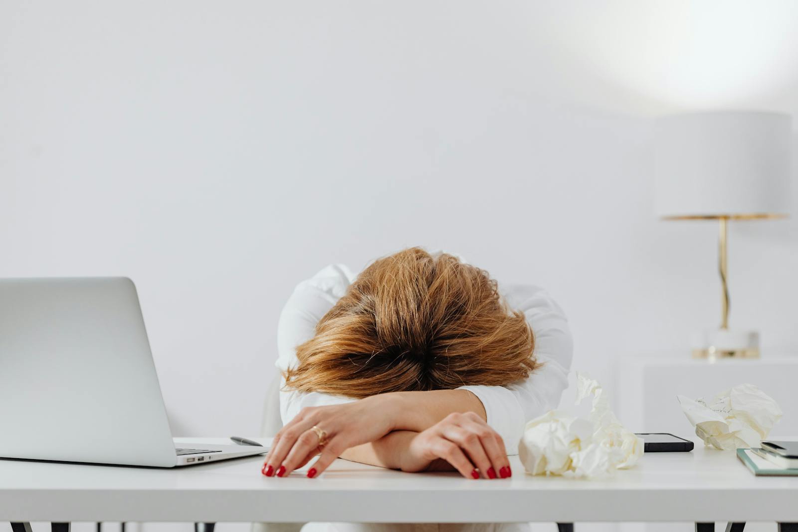 A woman resting her head on her arms beside a laptop, looking depleted