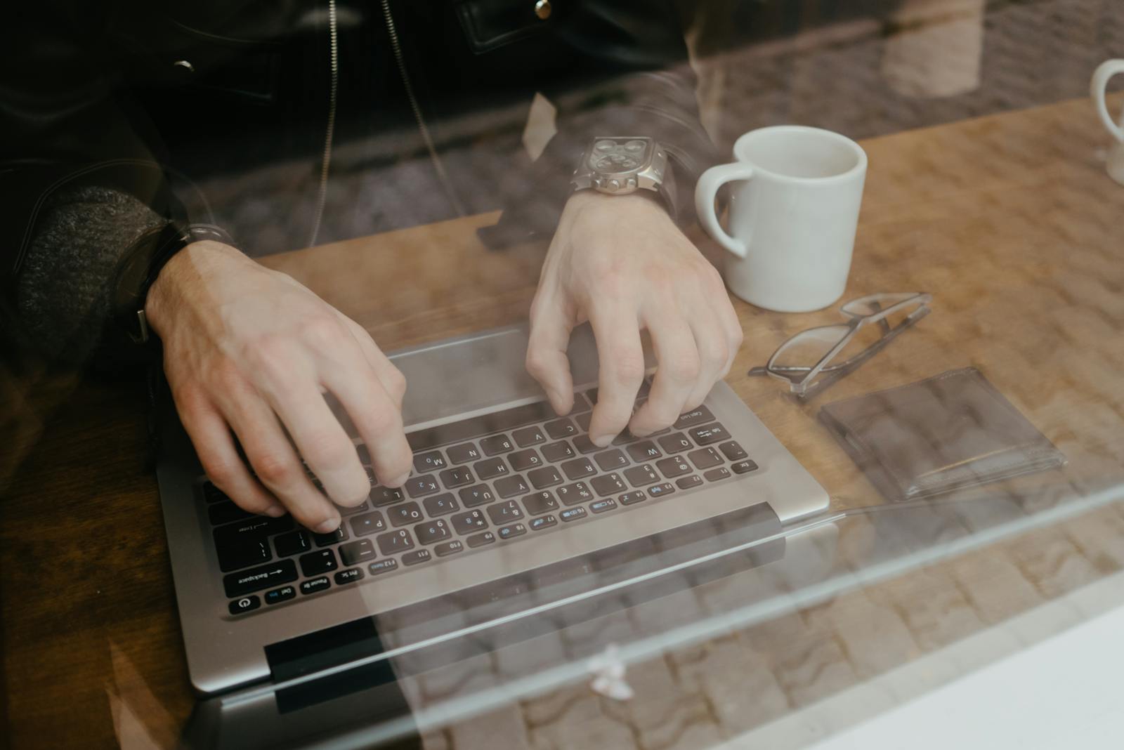 Hands typing on a laptop with a ceramic mug nearby — working through imposter syndrome