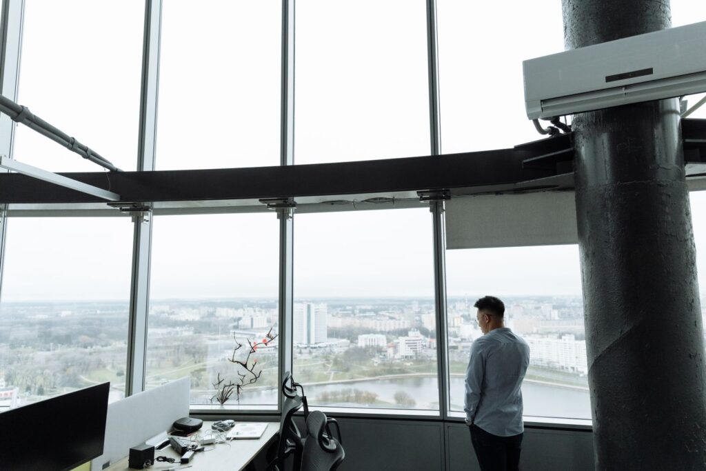 Professional standing alone by a glass office window — high-achievers and imposter syndrome